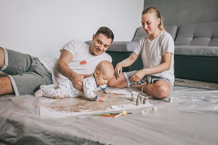 Young family with adorable infant child painting together on floor