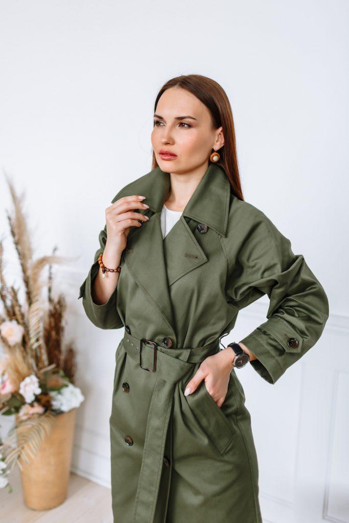 A model girl in a green raincoat. Clothing demonstration in a showroom.