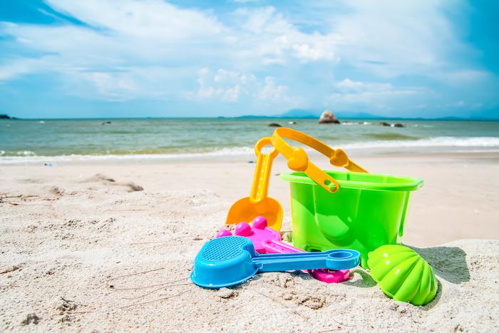 Child's bucket, spade and other toys on tropical beach against blue sky