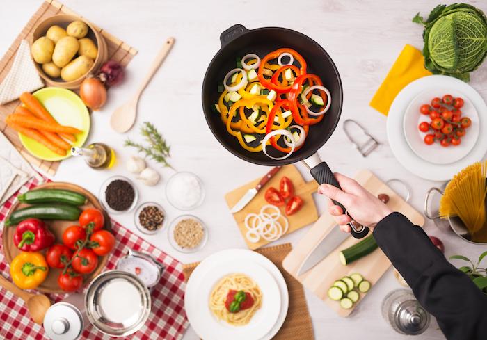 Professional cook frying fresh sliced vegetables in a nonstick pan hands close up, food ingredients and kitchenware on background, top view