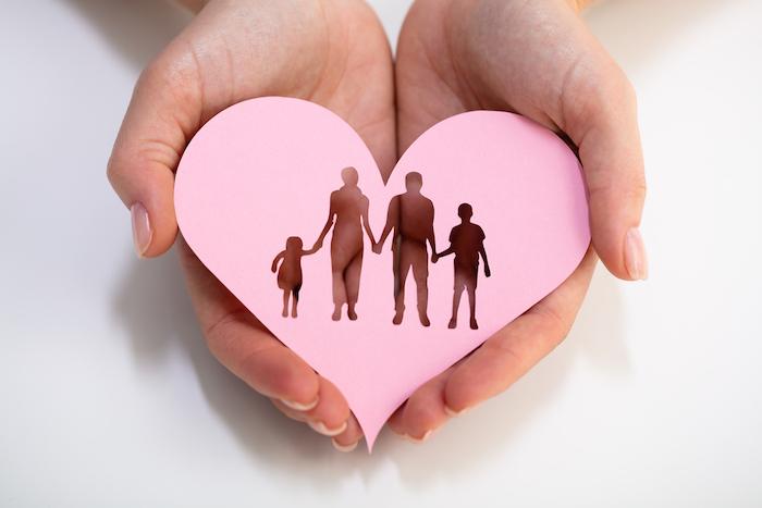 An Overhead View Of Person's Hand Holding Family Cut Out On Red Heart