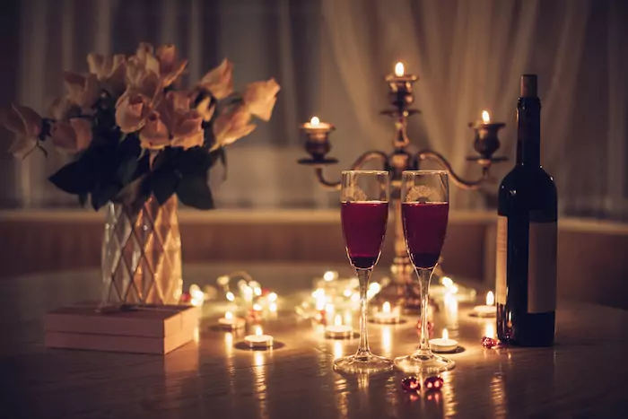 Candlelight date. Glasses with wine candles bouquet of rose and gift box on table. Romantic candlelight dinner at home at night