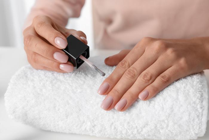 Woman applying nail polish at table, closeup. At-home manicure