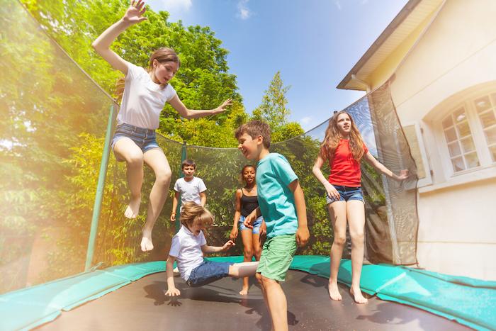Big group of happy children jumping on the outdoor trampoline and having fun during summer vacation