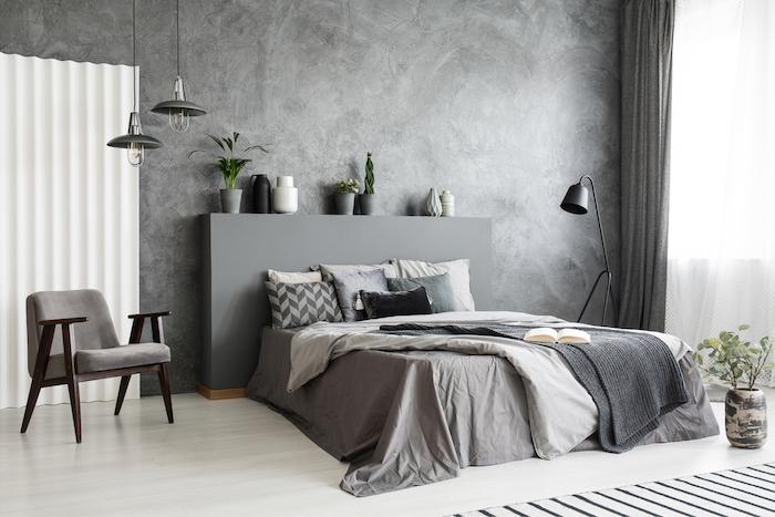 Modern grey bedroom interior with big bed with pillows and linen. Comfortable armchair next to the bed.