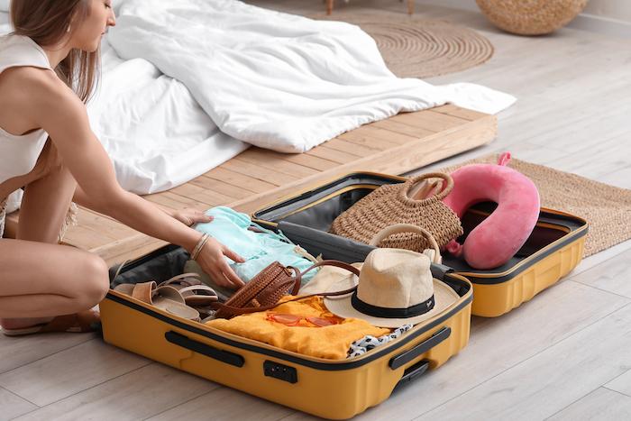 Young woman unpacking her summer clothes from suitcase in bedroom