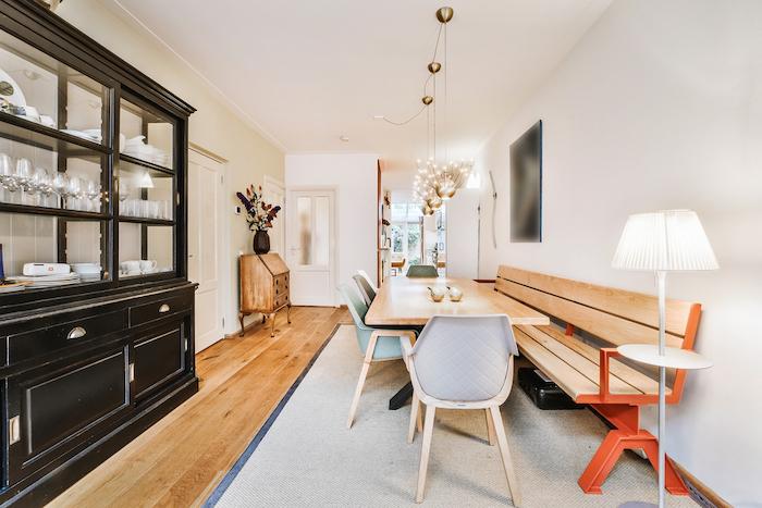 Modern design of apartment dining room with wooden table and chairs with bench under pendant lamps