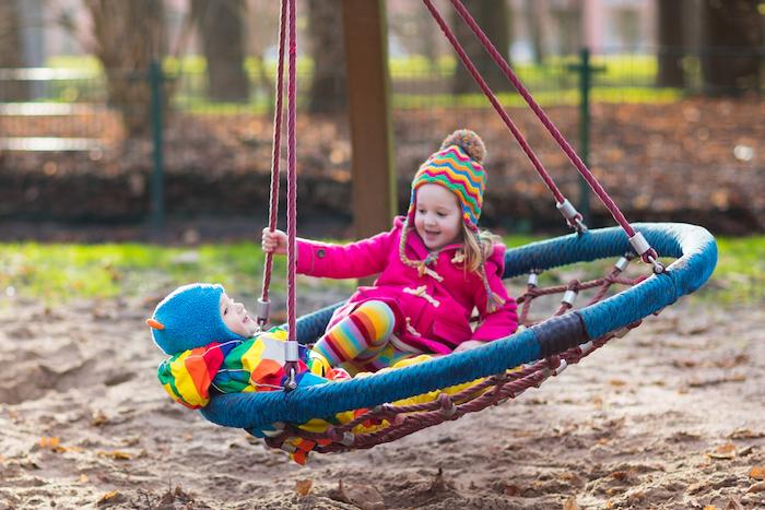 Children having fun on cold weather day. Toddler on a swing.