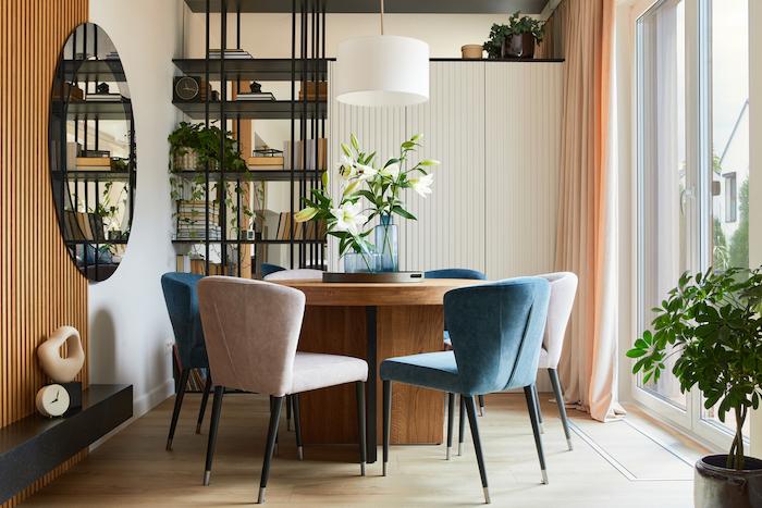 Stylish composition of elegant dining room interior design with velvet armchairs, design rouded wooden table and beautiful personal accessories