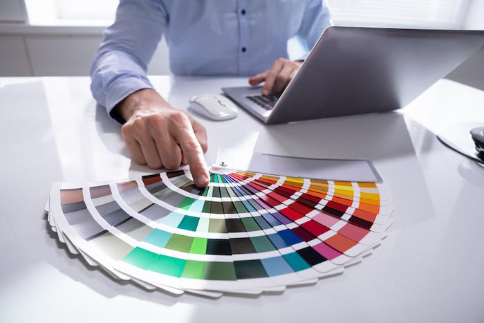 Cropped image of male designer holding color swatches while using laptop at desk