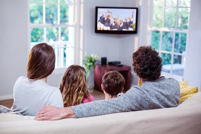 Family watching television while sitting on sofa at home - 5 TV Moments That Connect Us