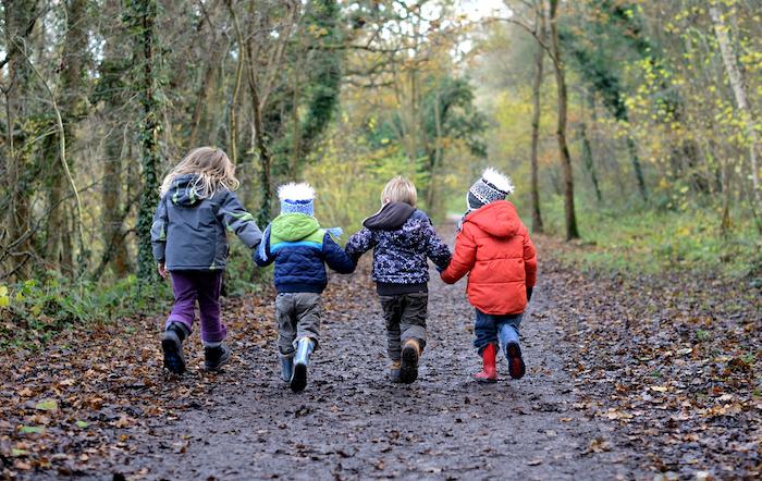 four children holding hands walking down a wooded path having fun