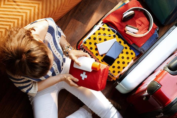 Woman packing first aid kit and SPF in open travel suitcase