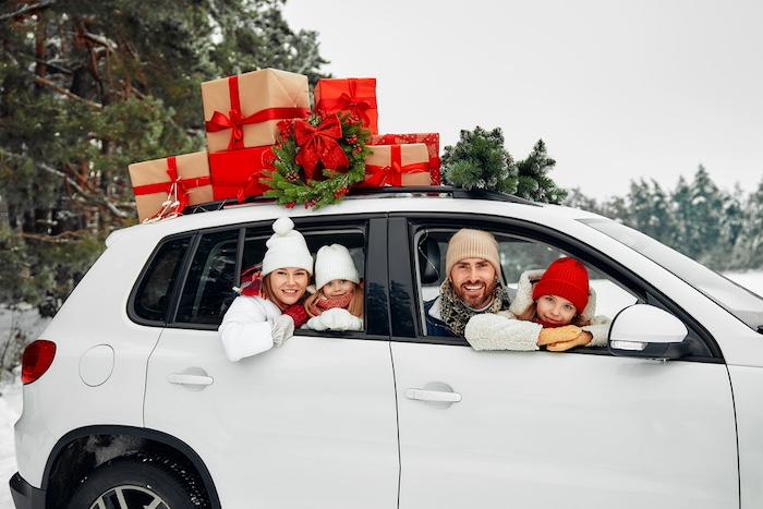 Holiday Season Survival for a Stress-Free Family Visit.Merry Christmas and Happy New Year. Happy family with children sitting in a car loaded with boxes of gifts and a Christmas tree against the background of a forest in snowy weather.