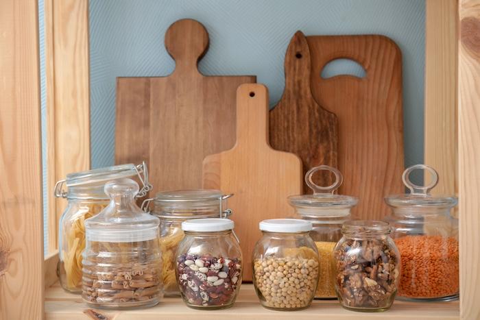 Glass jars with different foodstuff and cutting boards on shelf indoors
