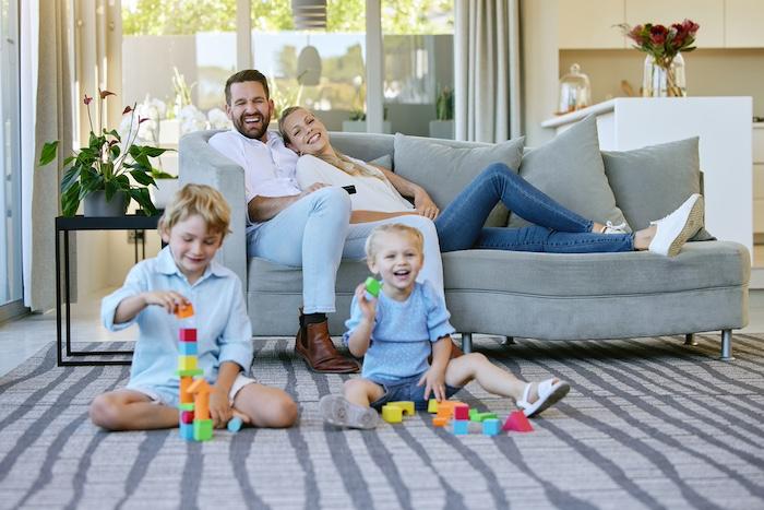 Simple Systems to Help Busy Parents Create a Stress-Free Home. Full length shot of an affectionate family of four relaxing in the living room at home.