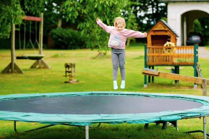 Little preschool girl jumping on trampoline. Happy funny toddler child having fun with outdor activity in summer. Sports and exercises for children.