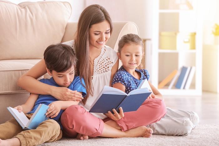 Young woman and her little children reading books at home