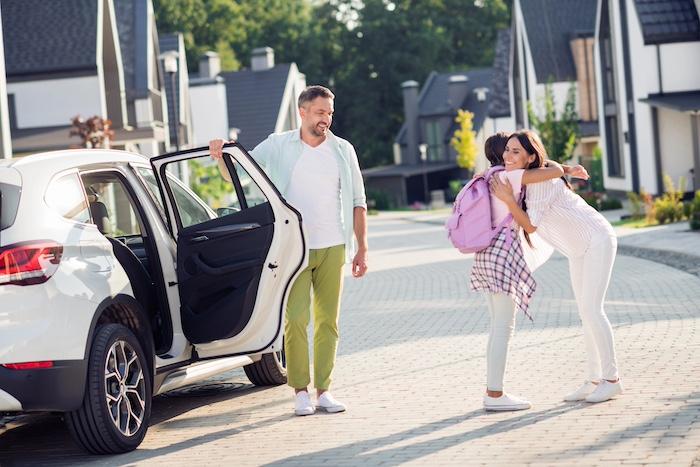 Helping Children Transition Smoothly Between Two Homes. Photo portrait of girl hugging mother coming back from spending time with father exiting white car outdoors.