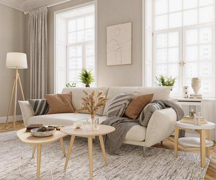 Cosy Home Tips - How to Make Your Home Warm & Inviting. Bright living room interior design with windows and beige walls is furnished with modern sofa, armchares, floor lamp, coffee table and other decorative elements.