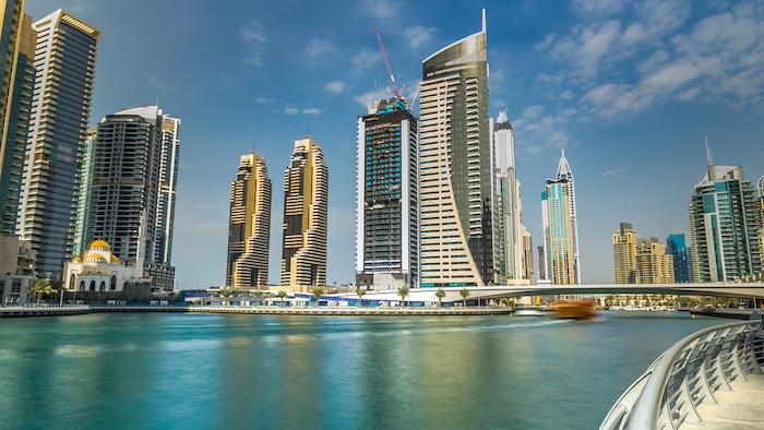Dubai Marina modern towers with floating yachts and boats from promenade timelapse, United Arab Emirates. Tallest skyscrapers skyline. Blue cloudy sky