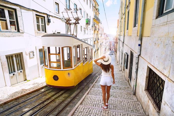 Woman tourist walking in narrow streets of Lisbon city old town. Famous retro yellow funicular tram on a sunny summer day. Tourist attraction.
