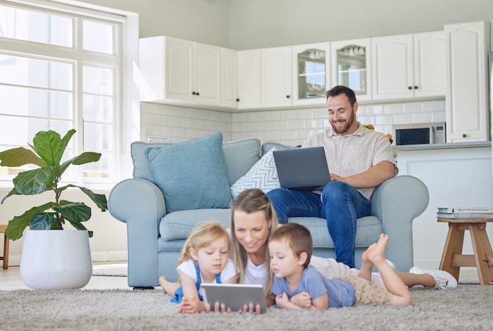 The Essential Family Checklist Before Upgrading Your Home Internet Plan. Caucasian man working from home with his family. Mother reading on a tablet with her children. Father and mother in the lounge with the children. caucasian family using tech devices together