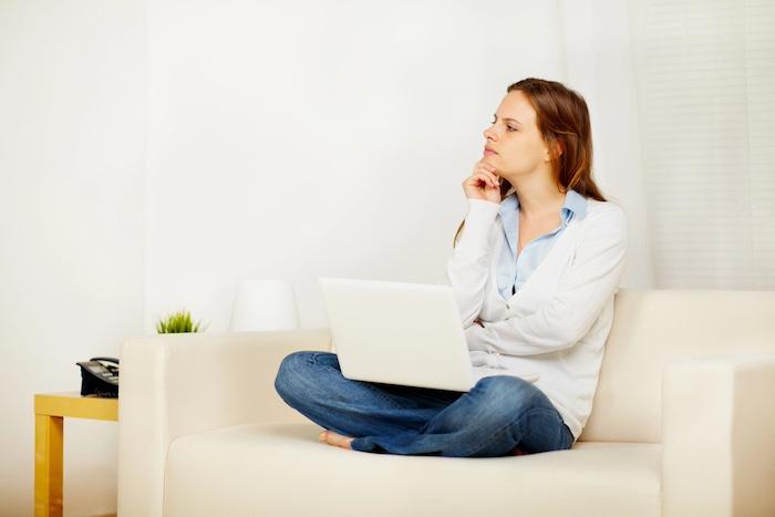 Portrait of a young lovely female thinking on sofa and holding a laptop while resting