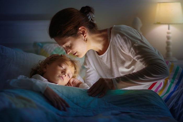 Child sleeping in dark bedroom. Little boy napping. Healthy night rest. Kids room with night light. Toddler with teddy bear. Bedding for children.