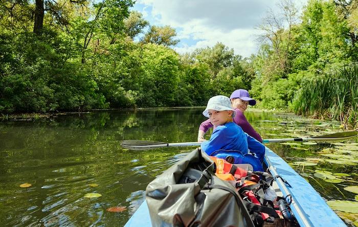 Mother and child kayaking on a calm river surrounded by lush green forest. Family adventure with paddles, water lilies, and outdoor summer recreation in nature.