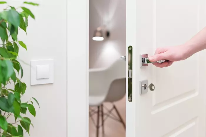 To open the door. Modern white door with chrome metal handle and a man's arm. Elements of interior closeup.