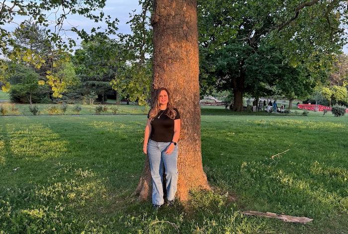 Franca wearing wide leg jeans, black top posing outdoors at the park in front of a tree