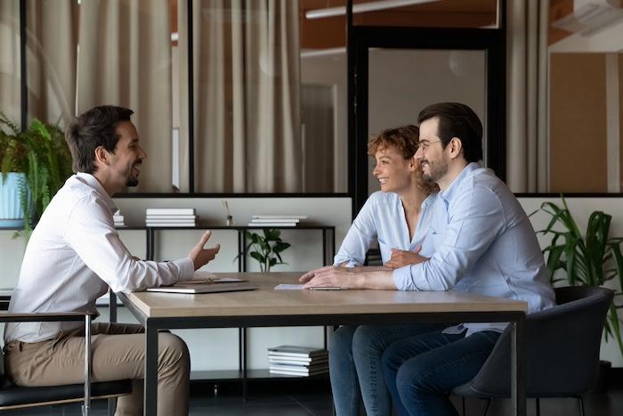 Happy family couple of clients meeting with real estate insurance agent, consulting realtor, broker, lawyer about mortgager, loan, house buying or rent, discussing contract terms in office