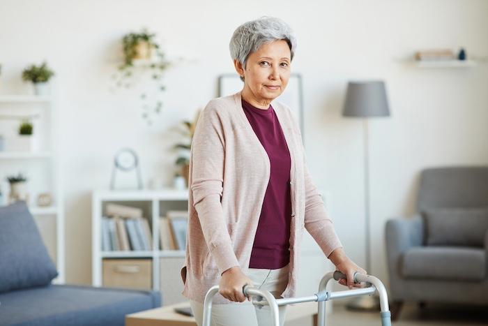 Senior woman leaning on the walker and looking at camera while standing in the room