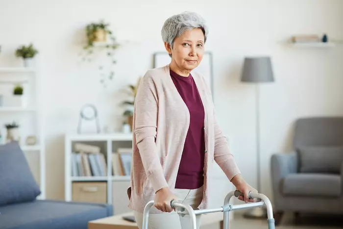 Senior woman leaning on the walker and looking at camera while standing in the room
