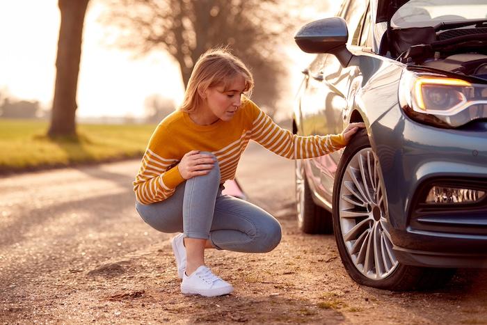 Woman Broken Down On Country Road Checking Car Tyre