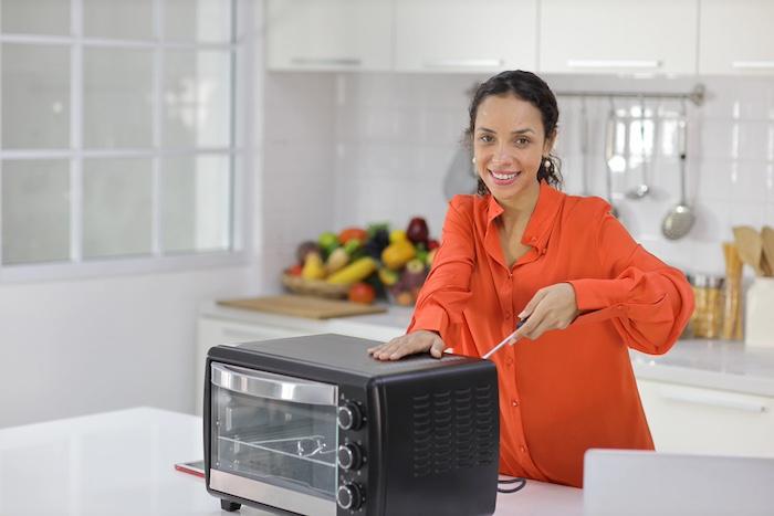 Happy Latin woman repairing and fixing microwave oven in kitchen.